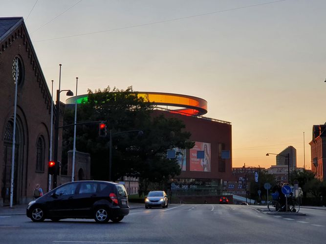 Das Aros Museum ist ein kubischer Neubau, der einen bunten Heiligenschein trägt. Dieser ist bunt durch neonleuchten.