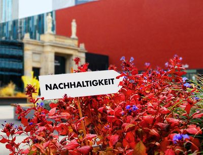 Zu sehen ist das Leibniz-Forum der Universität Leipzig, im Vordergrund ein Schild mit der Aufschrift "Nachhaltigkeit".