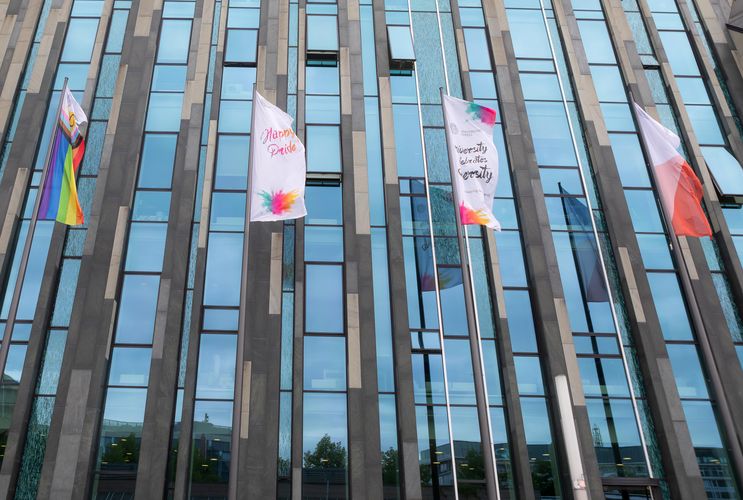 Ansicht der vier Flaggenmasten vor dem Neuen Augusteum. An einem der Flaggenmasten ist die Intersex Inklusive Pride Flagge, eine Flagge der Universität Leipzig soiwe zwei mit dem Aufdrukc "University celebrates diversity"
