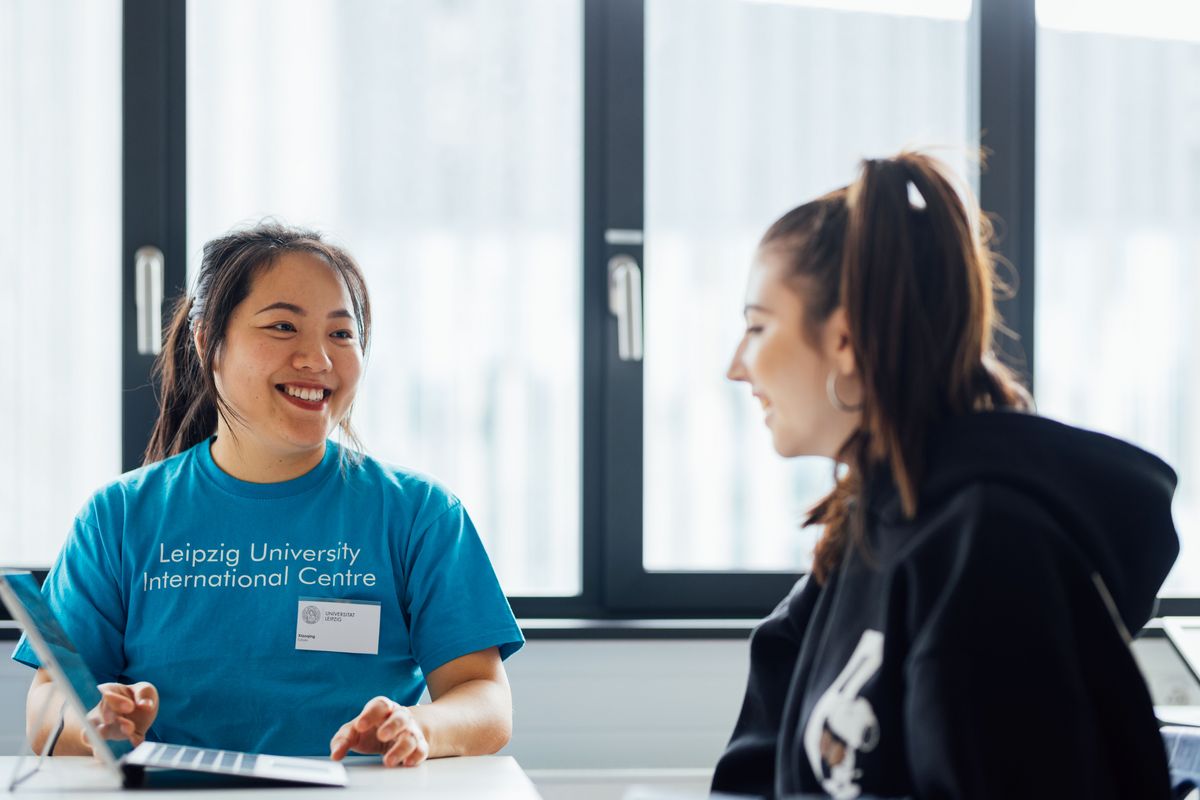 zur Vergrößerungsansicht des Bildes: Farbfoto: Eine Person der Universität Leipzig lächelt eine andere Person an und zeigt ihr Informationen auf einem Laptop