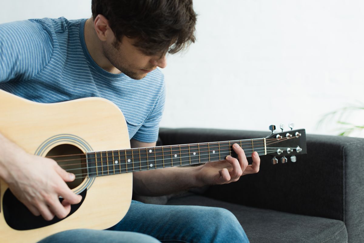 Man sieht einen jungen Mann, der konzentriert Gitarre spielt.
