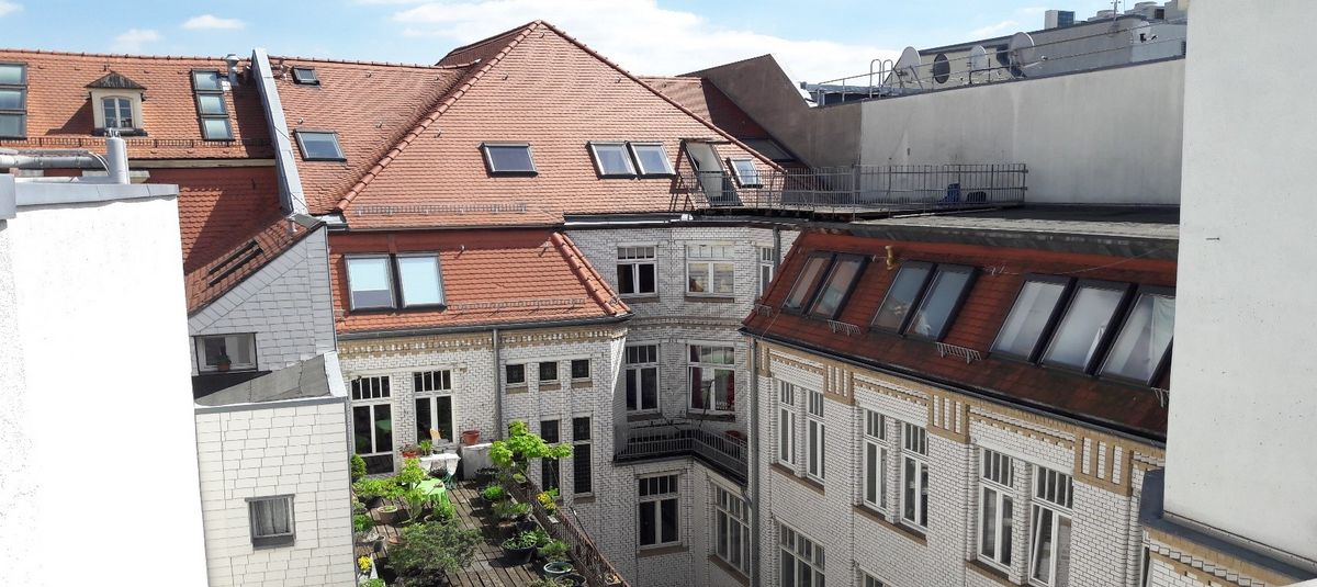 zur Vergrößerungsansicht des Bildes: Blick auf den Innenhof der Hainstraße 11 bei Sonnenschein: rot gedeckte Mehrfamilienhäuser mit weißer Fassade und teilweise begrünten Dachterrassen. Foto: Thomas Biermann