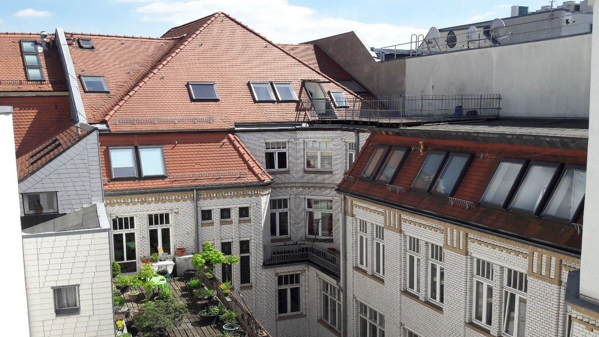 enlarge the image: Courtyard view of the guest house at Hainstraße 11 in sunlight: red-roofed apartment buildings with white facades and a greened roof terrace. Photo: Thomas Biermann.