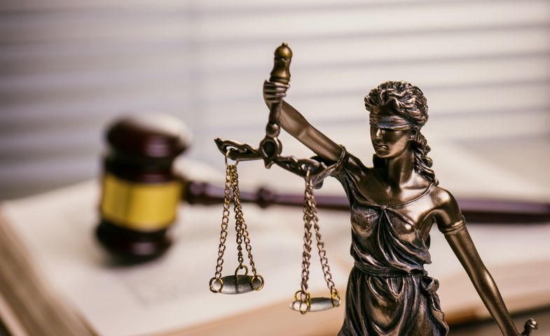 Figur der Justitia vor einem Richterhammer auf Gesetzesbuch