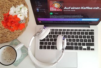 ein Laptop von oben, darauf liegt ein weißer Kopfhörer, daneben steht eine Tasse Kaffee