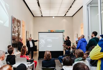 Professor Meijer erklärt in einer Ausstellung dem Publikum ein Exponat