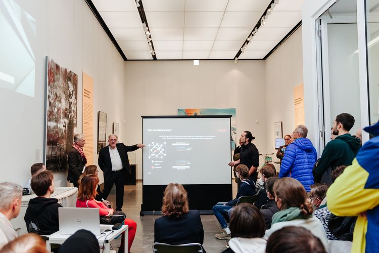 Professor Meijer erklärt in einer Ausstellung dem Publikum ein Exponat