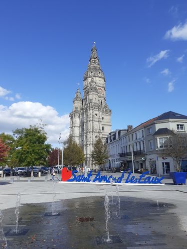 Farbfoto: Aufnahme eines Platzes mit Wasserfontänen und einem Aufsteller mit Herz und dem Namen der Stadt. Im Hintergrund befindet sich ein Turm mit Kuppeln und Verzierungen