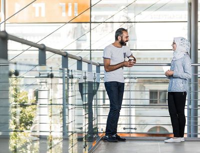 Two students talk in the bright stairwell of the Humanities Centre