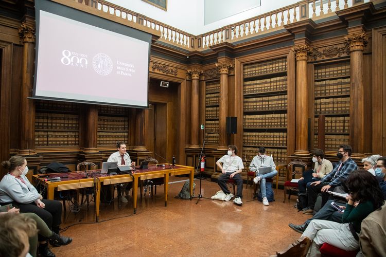 Menschen sitzen in großem Kreis zusammen in einem altehrwürdigen Raum, der an eine Bibliothek erinnert