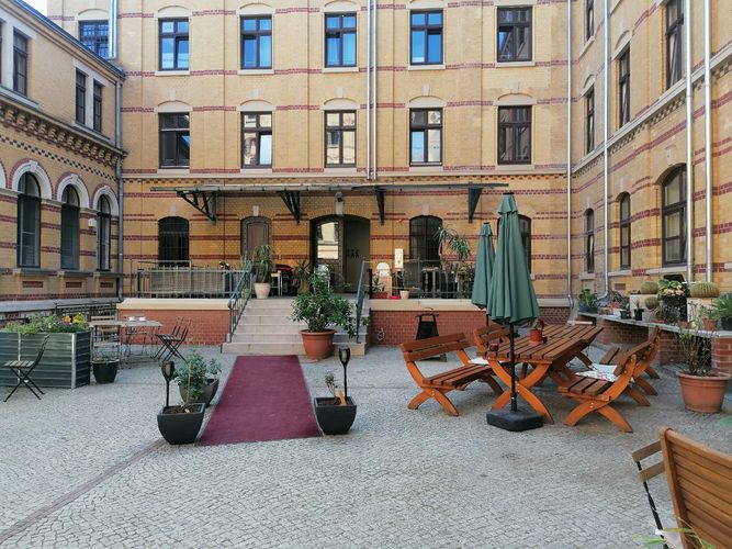 [Translate to English:] Tables, benches and chairs arranged for an ouside seating area of a cafe surrounded by buildings