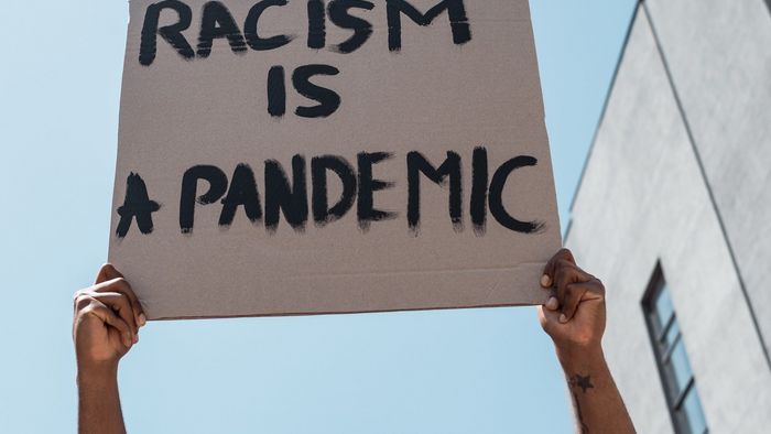 Zu sehen ist ein Demonstrant, der ein Plakat hochhält: "Racism is a Pandemic"