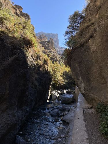 Felsen sind am linken und rechten Bildrand zu sehen. In der Mitte des Bildes führt ein kleiner Fluss durch die felsige, wüstenähnliche Landschaft.