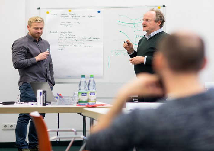 Dozent und Student stehen am Flipchart in einem Seminarraum.