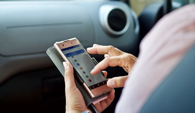 Eine Frau sitzt auf dem Beifahrersitz eines Autos, in der Hand hält sie ihr Smartphone.