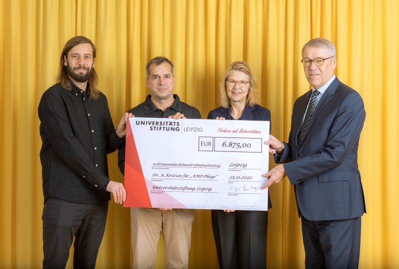 zur Vergrößerungsansicht des Bildes: Farbfoto: Prof. Dr. Birgit Dräger, Dr. Hubert Temmeyer und Prof. Dr. Harald Krautscheid von der Universitätsstiftung überreichen den symbolischen Scheck an den Fördermittelempfänger Dr. Andor Krizsan