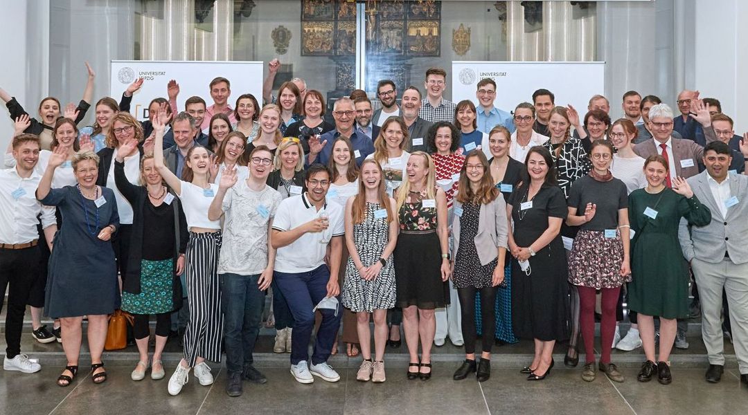 Farbfotografie: Gruppenbild von Förderern und Stipendiaten des Studienganges Pharmazie. Ungefähr 50 Personen stehen in mehreren Reihen hintereinander und winken in die Kamera