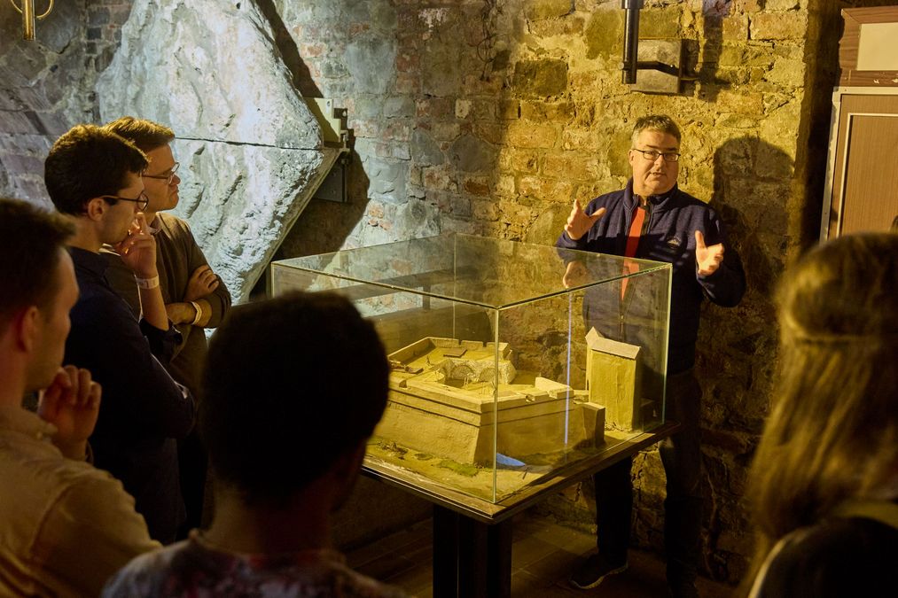 zur Vergrößerungsansicht des Bildes: Förderer und Stipendiaten stehen im Oberkeller der Moritzbastei um eine Vitrine mit dem Modell der Moritzbastei und hören dem Gästeführer zu