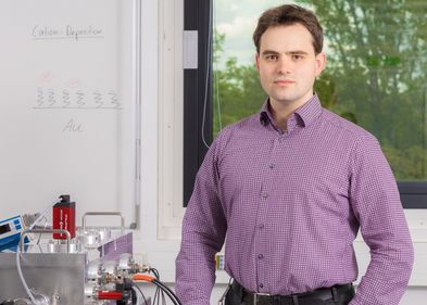 Mann steht vor einem Fenster, neben ihm Laborgegenstände