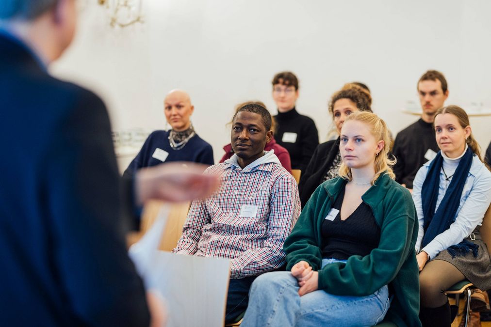 zur Vergrößerungsansicht des Bildes: Viele Menschen sitzen in einem hellen Raum