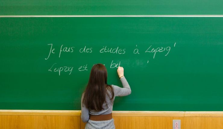 Frontalsicht auf eine Dozentin, die gerade etwas auf eine große grüne Tafel schreibt, die das ganze Foto einnimmt, Foto: Christian Hüller