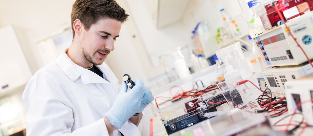 Ein männlicher Forscher führt ein biochemisches Experiment im Labor durch und arbeitet mit einer Pipette und Reagenzgläsern.