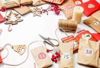 Forbfoto: Auf einem Tisch liegen Schere, Zwirn, verschiedene Weihnachtsanhänger aus Holz und einige kleine Papiertüten mit Zahlen für den Adventskalender darauf.