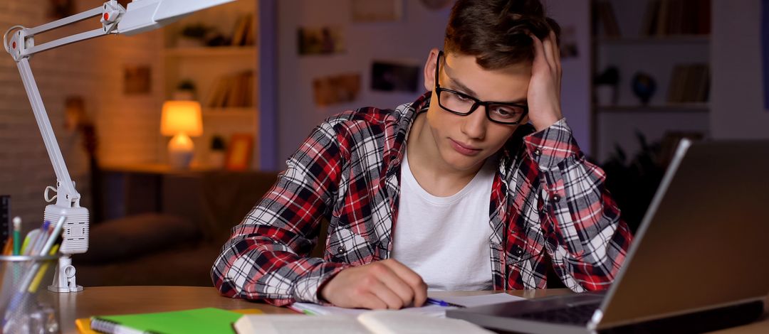 Ein junger Student sitzt verzweifelt am Schreibtisch, während er seinen Kopf mit der Hand stützt. Foto: Colourbox