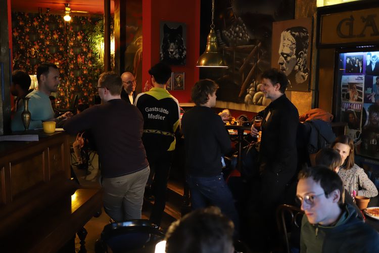 Five pairs of people sitting or standing and chatting in a cafe