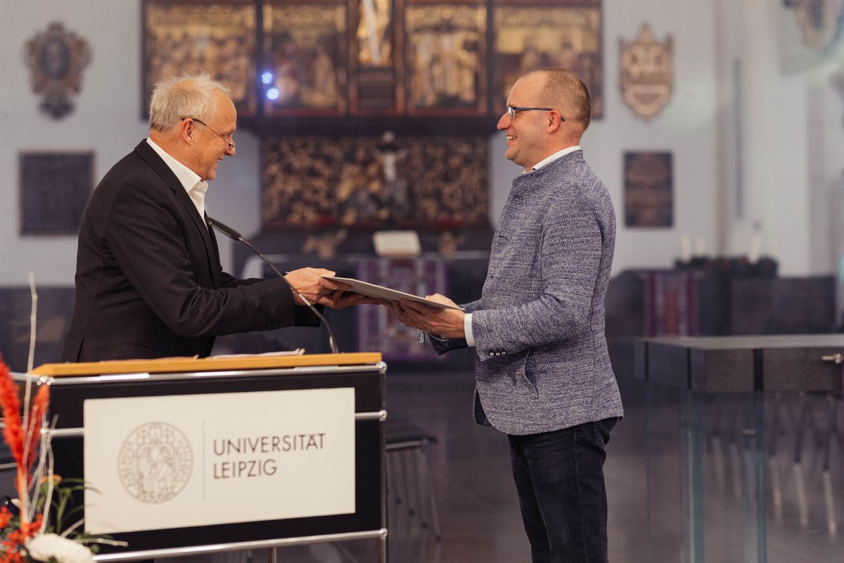 zur Vergrößerungsansicht des Bildes: Prof. Dr. Thomas Lenk steht rechts im Bild. Er überreicht die Urkunde an Prof. Dr. Utz Dornberger und gratuliert ihm. Prof. Dr. Utz Dornberger steht links im Bild