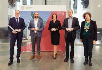 Preisträger der Universitätsmedaille posieren im Paulinum vor einem Banner der Universität zusammen mit der Rektorin Beate Schücking