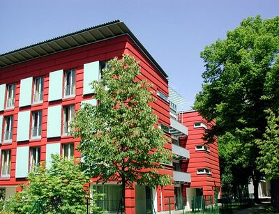 Rote Fassade des Werner-Heisenberg-Hauses der Universität. Die Bäume vor dem Gebäude lassen erahnen, dass es in einer besonders grünen Umgebung steht.