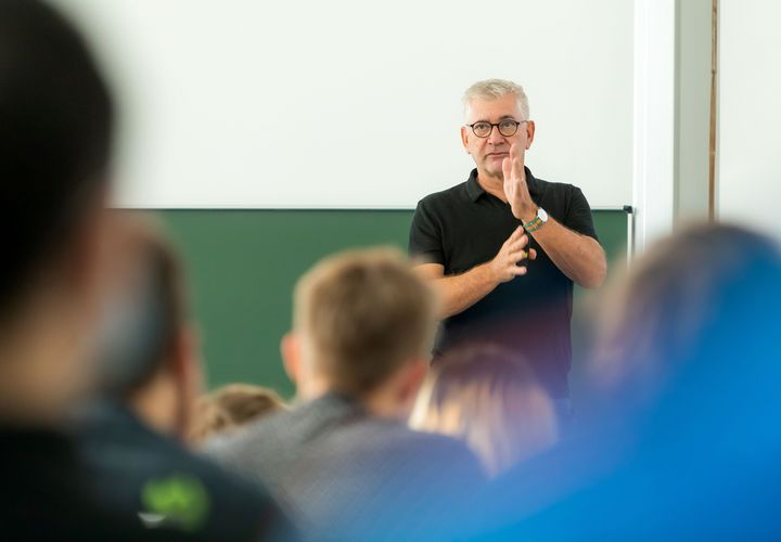 A man standing in front of the audience talking and explaining with his hands
