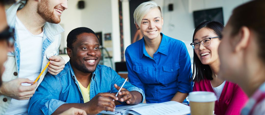 Internationale Studierende sitzen gemeinsam an einem Tisch, lernen und unterhalten sich. Sie lachen dabei.