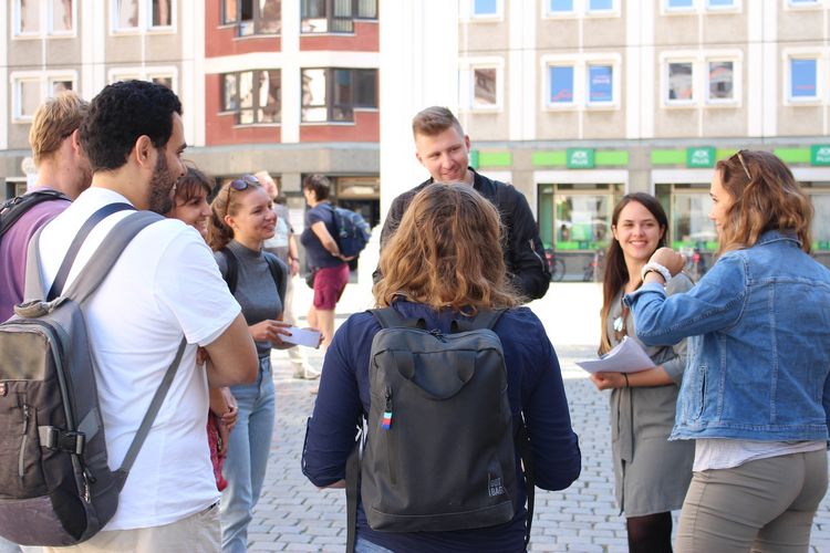 A group of young people are stood outside talking on a public square.