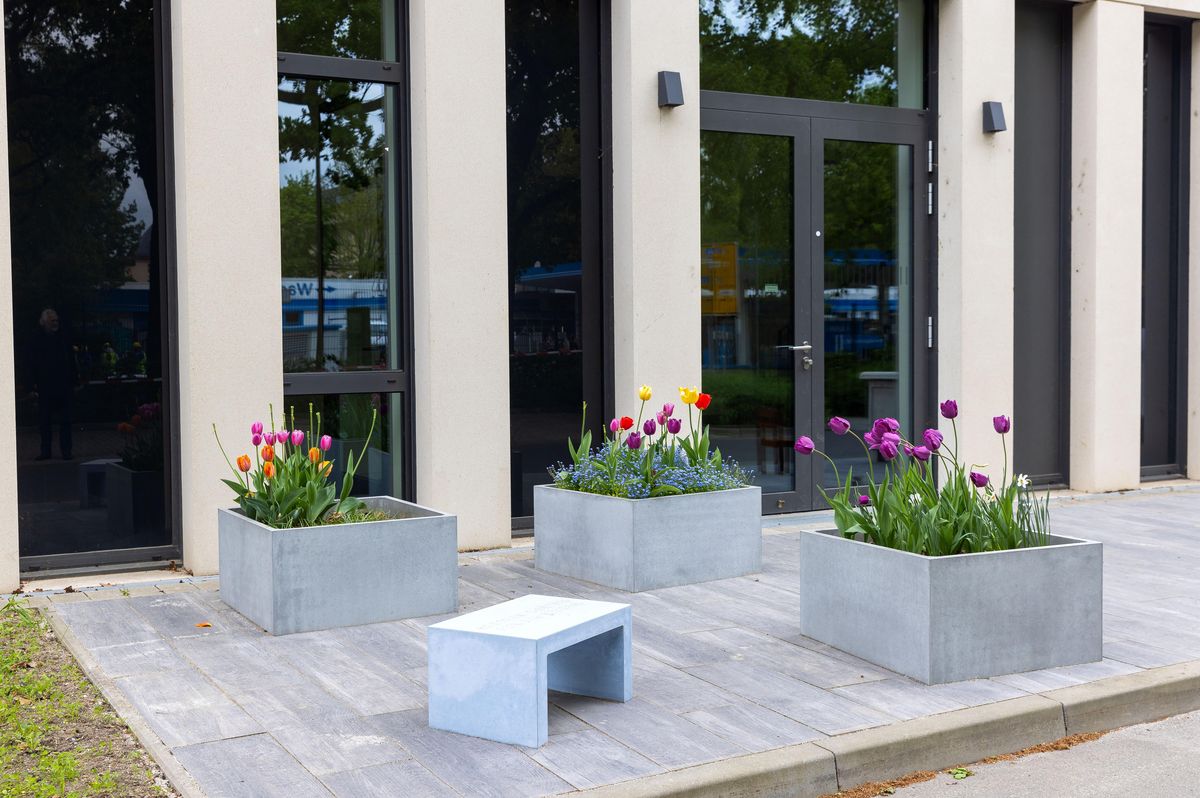 zur Vergrößerungsansicht des Bildes: Ansicht des Mahnmals "Der Garten der Kinder". 3 mit Tulpne bepflanzte Kübel. Im Vordergrund eine kleine Betonbank