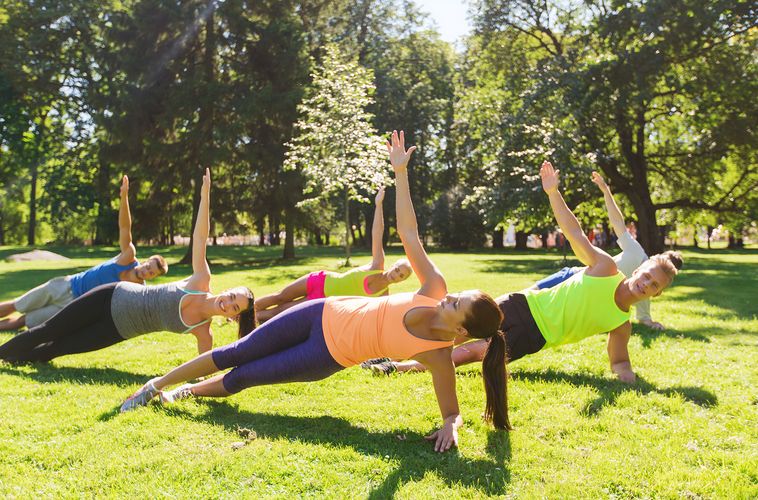 mehrere Menschen machen sportliche Übungen auf einer sommerlichen Wiese in einem Park