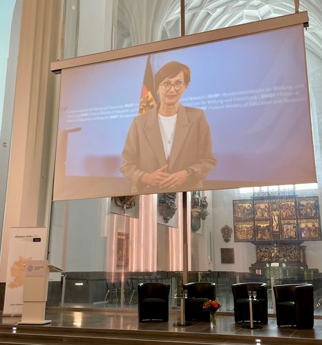 Bundesministerin Bettina Stark-Watzinger auf einer Video-Leinwand im Paulinum.