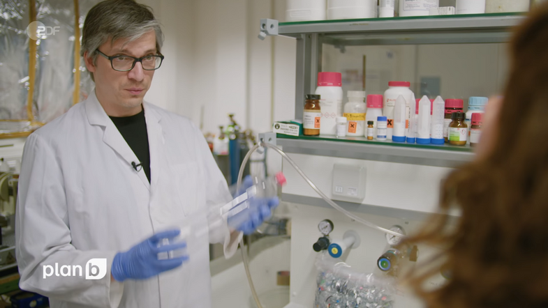 Dr. Christian Sonnendecker im Interview in einem Labor mit einer PET-Flasche in der Hand