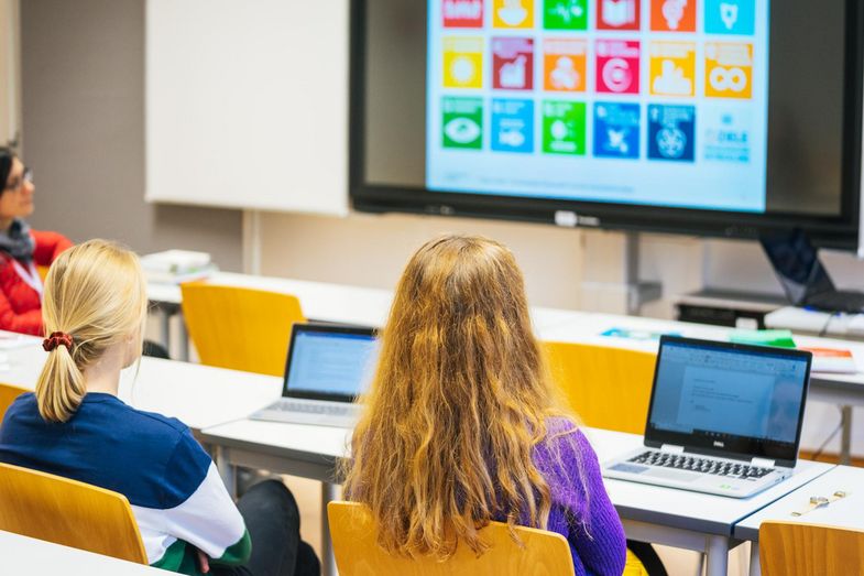 Junge Menschen sitzen in einem Unterrichtsraum an Laptops