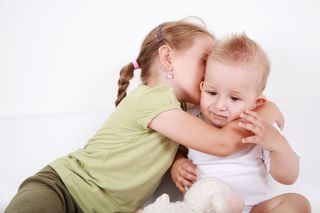 Auf dem Bild ist ein kleiner Junge zu sehen, der von seiner älteren Schwester umarmt wird.