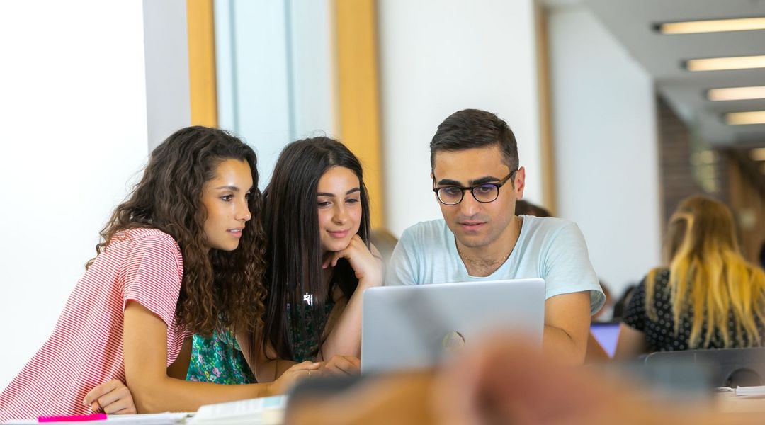 Zu sehen sind drei Studierende, die gemeinsam auf einen Laptop schauen.