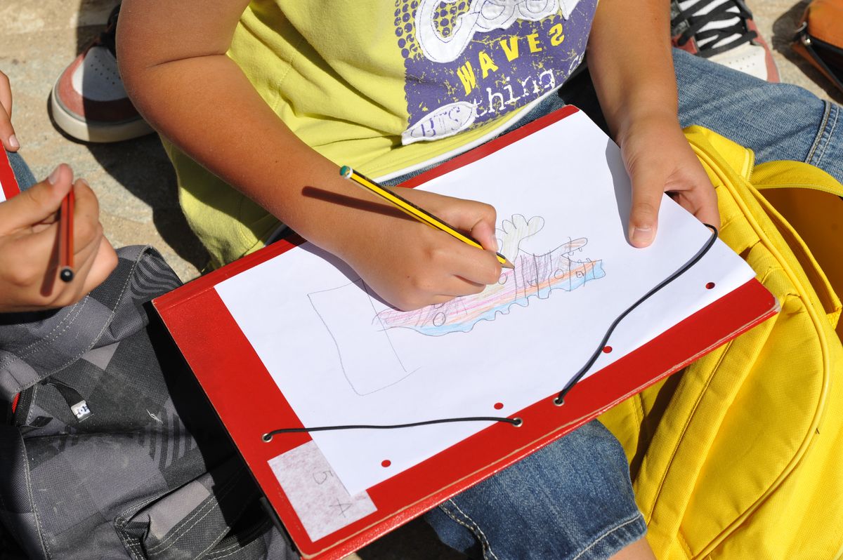 Das Bild zeigt ein Kind, das auf ein weißes Blatt Papier mit Buntstiften malt