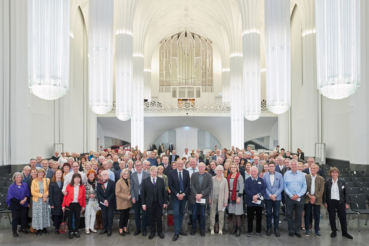 zur Vergrößerungsansicht des Bildes: alle zur Veranstaltung anwesenden Stuhlpatinne und Stuhlpaten stehen nebeneinander in der Aula des Paulinums für ein Gruppenbild, im Hintergrund ist die Empore mit der Jehmlich-Orgel zu sehen