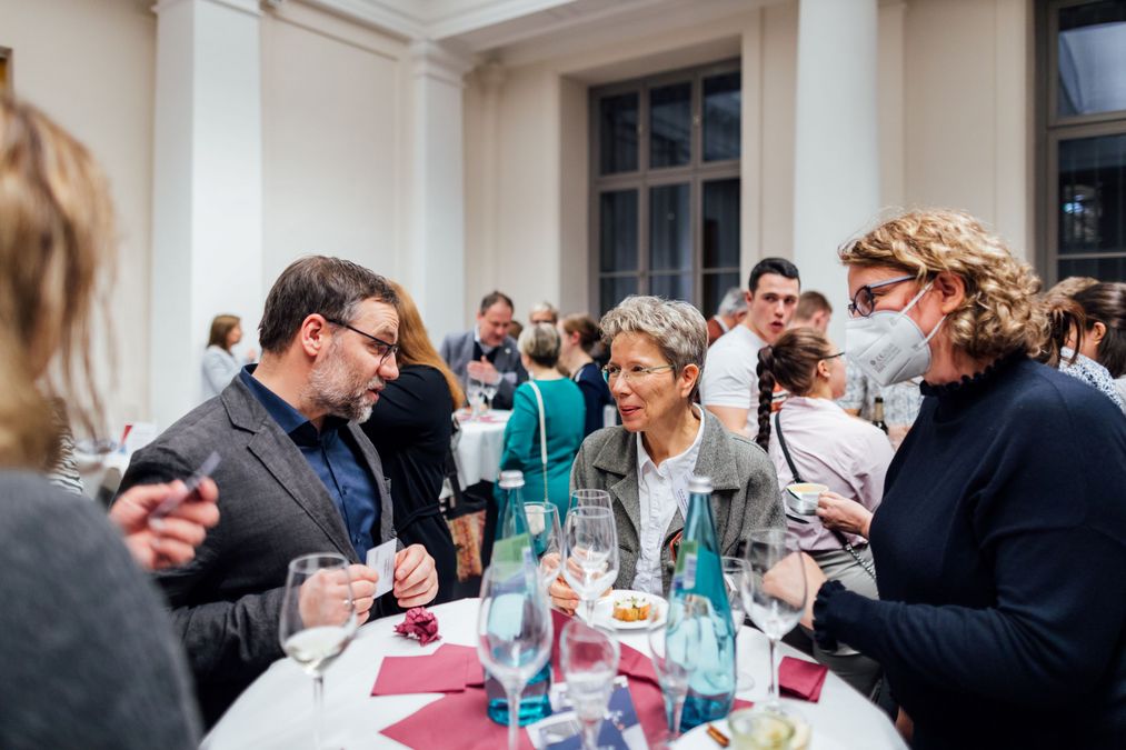 zur Vergrößerungsansicht des Bildes: Förderer und Professoren aus dem Netzwerk Deutschlandstipendium stehen an Stehtischen und unterhalten sich