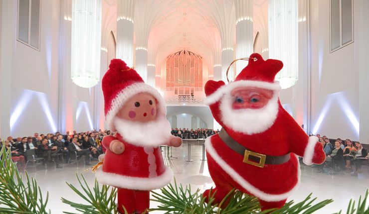 Zwei kleine Weihnachtsmannfiguren stehen Tannenzweigen. Im Hintergrund ist unscharf das Paulinum zu sehen.