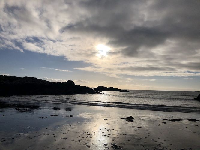 Zu sehen ist das Meer. Auf der linken Bildhälfte befinden sich Klippen. Die Sonne geht unter.