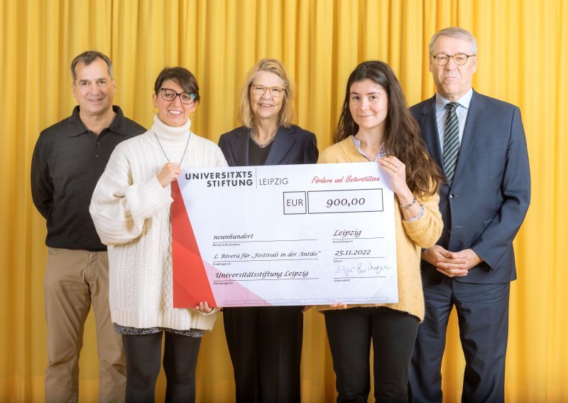 zur Vergrößerungsansicht des Bildes: Farbfoto: Prof. Dr. Birgit Dräger, Dr. Hubert Temmeyer und Prof. Dr. Harald Krautscheid von der Universitätsstiftung überreichen den symbolischen Scheck an die Fördermittelempfängerinnen Letizia Rivera und Martina Landrino