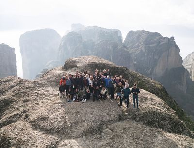 A group of people posing for the camera on a rock formation, imposing mountains in the background
