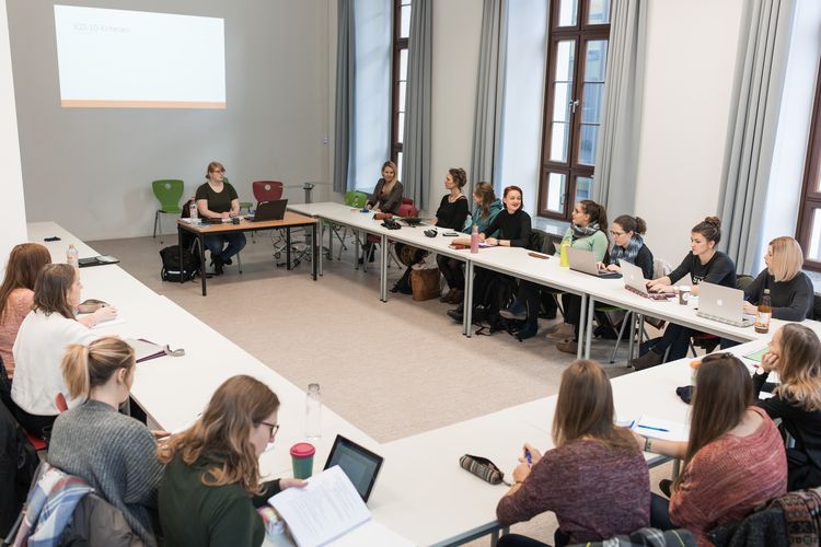 Studierende sitzen in einem Seminarraum an Tischen, die in einem U angeordnet sind, Foto: Christian Hüller